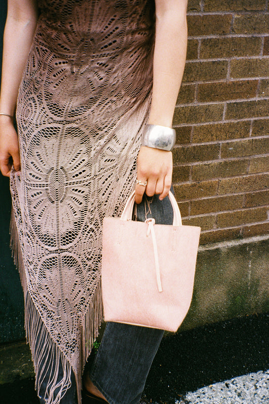Person holding a pink clutch with a patterned skirt and a silver bangle.