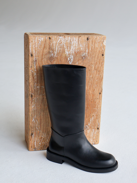 Black knee-high boot on a wooden block against a light gray background
