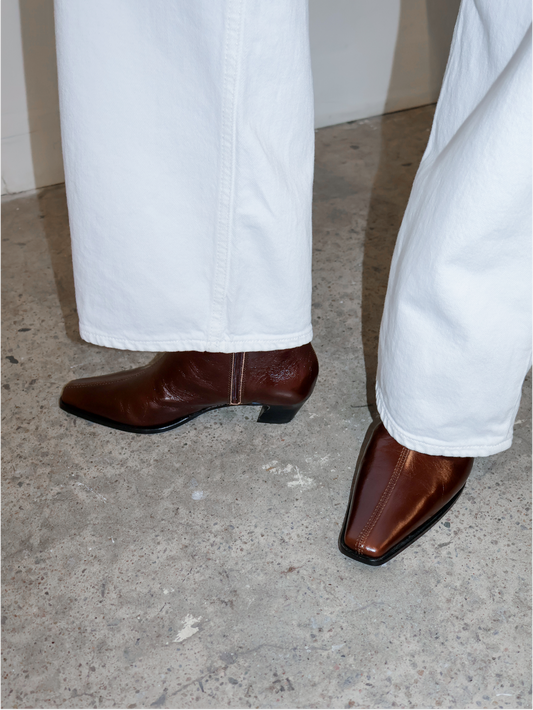 Brown leather boots worn with white pants on a concrete floor.