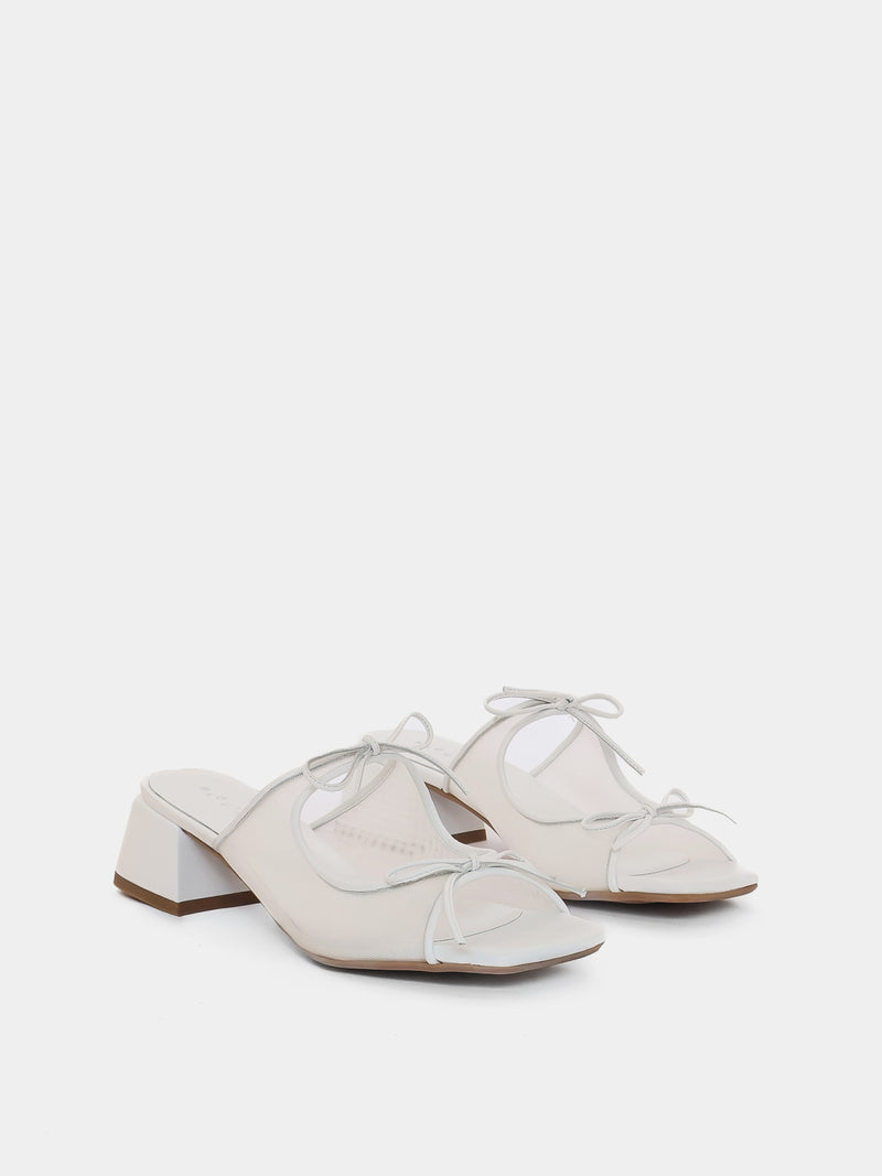 Pair of white shoes with a block heel on a light gray background