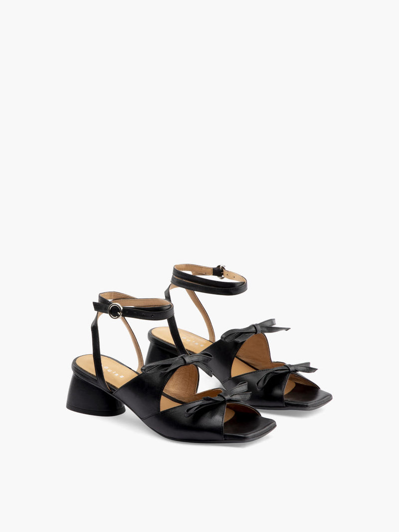 Black leather heels with two straps adorned with bows and an ankle strap