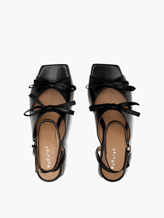 Black leather heels with two straps adorned with bows and an ankle strap