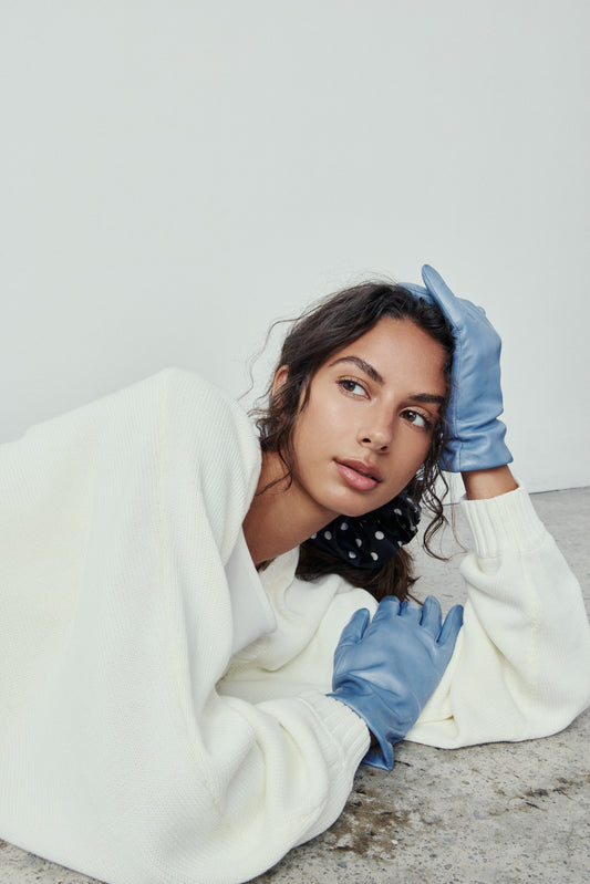 Person wearing a white sweater and blue gloves on a plain background