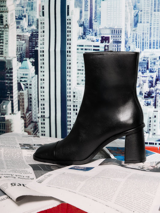 Black ankle boot on a newspaper with a cityscape background