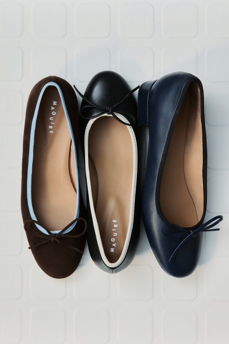 Three pairs of flats in brown, black, and navy on a light wooden surface.