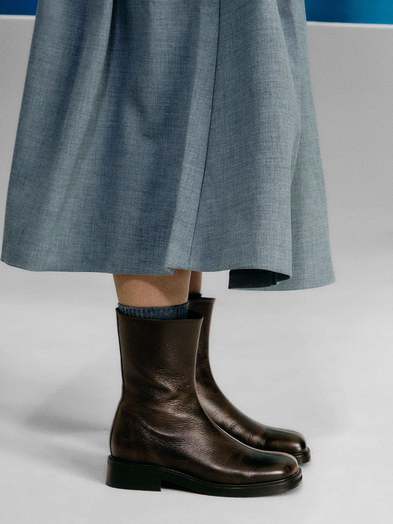 Brown boots worn with a light blue skirt on a neutral background