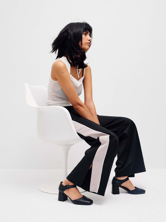 Model sitting on a white chair dressed in black and white with heel shoes.
