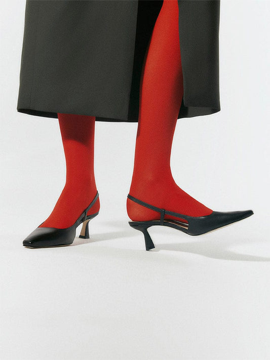 A black pointy toe pump with red tights and a black long skirt on model