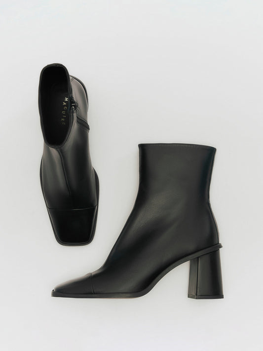 A black heeled boot with a square toe on a white background