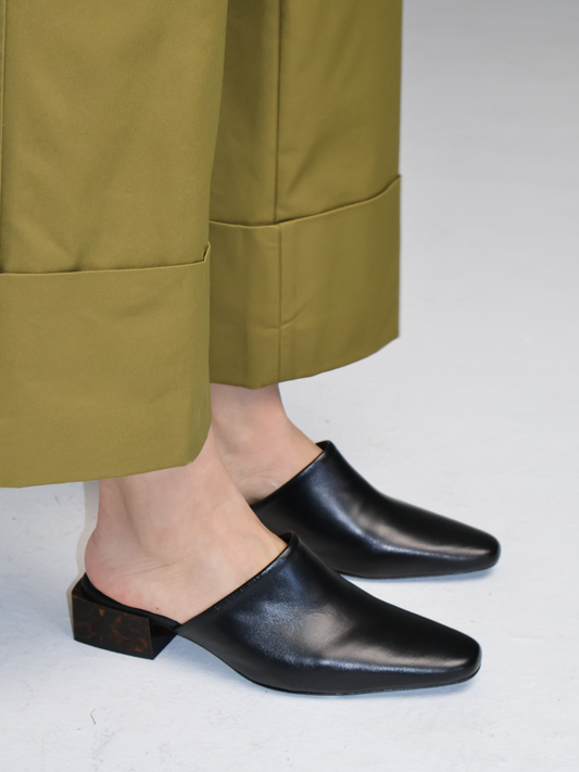 Person wearing black mule with green pants on a light gray background