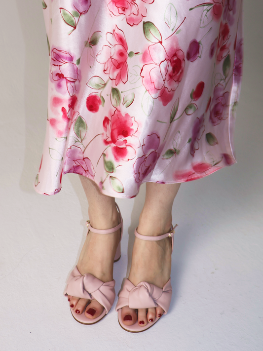 Woman with red pedicure wearing open toe pastel pink heels with a pink dress with flowers on white background.