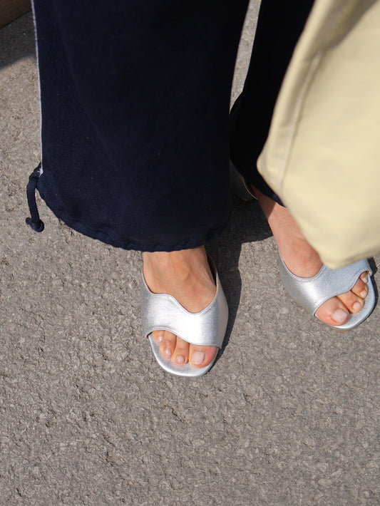Silver sandals worn on a gray pavement
