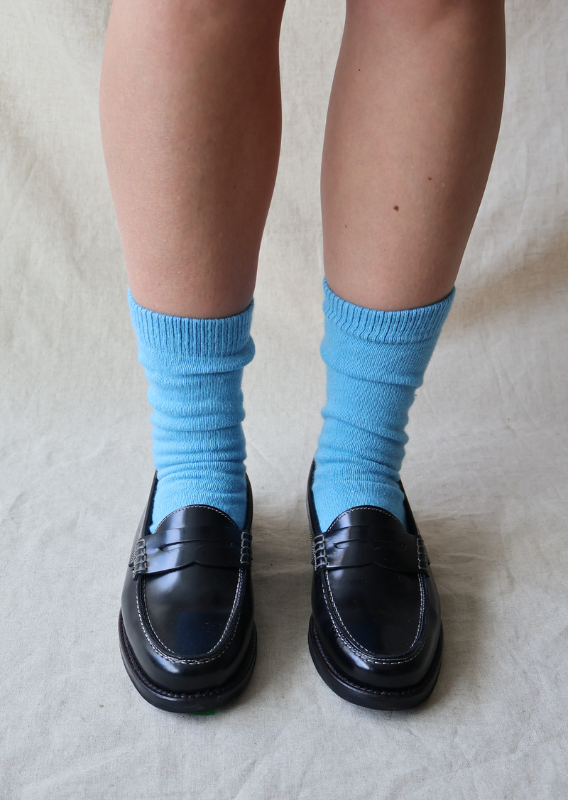 Person wearing blue socks and black shoes on a light background