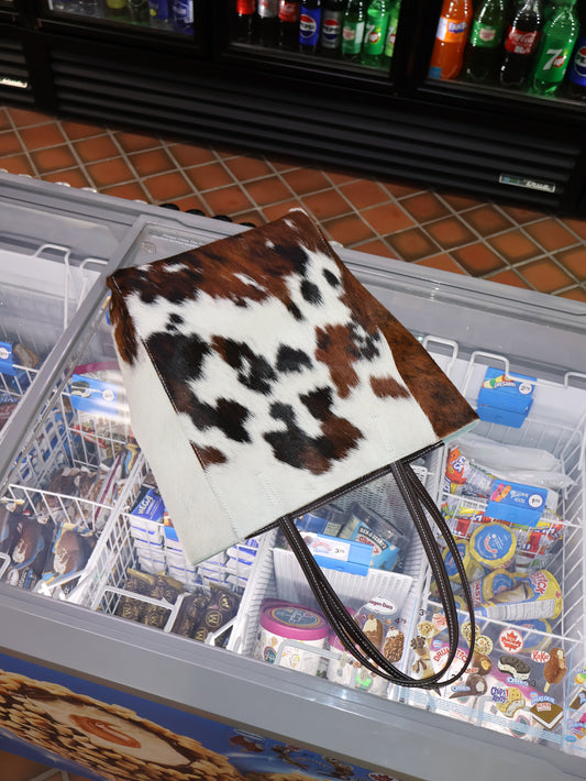 cow-patterned bag against the top of a corner shop fridge with popsicle inside.