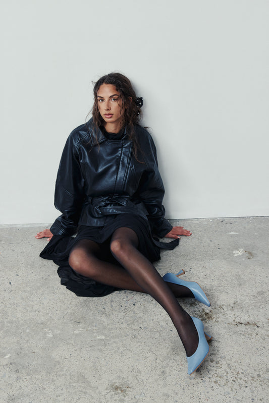 Woman sitting on a concrete floor wearing a black outfit with blue shoes.
