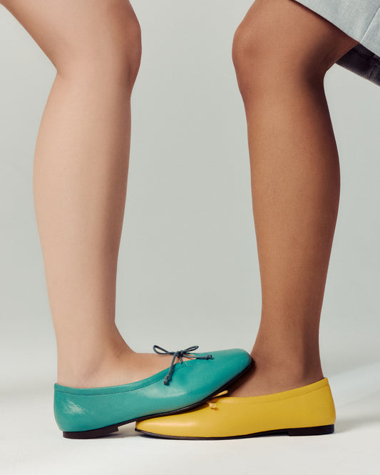 One foot wearing turquoise ballet flat stepping on other foot wearing same ballet flat in bright yellow. On white background in studio.