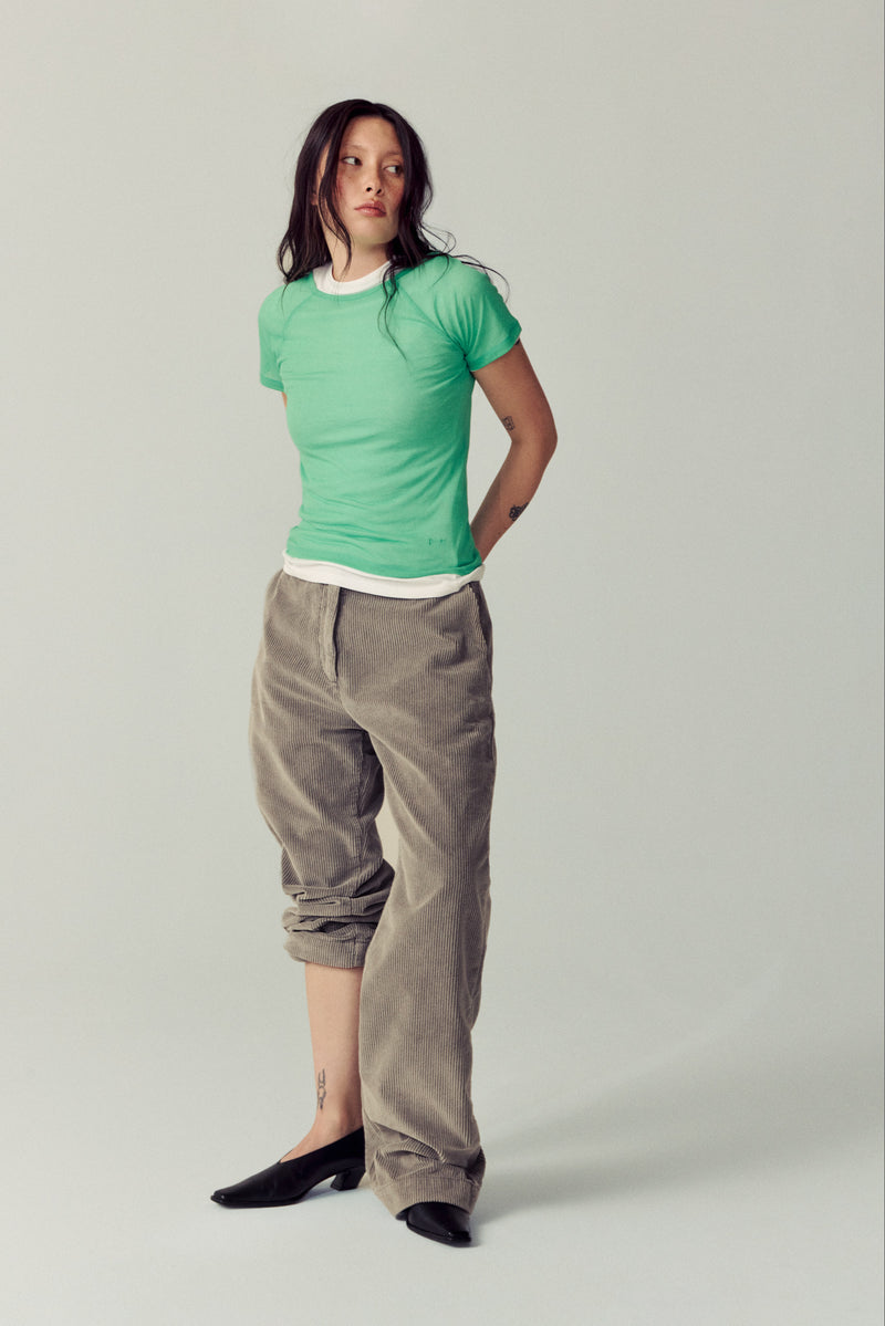 girl wearing corduroy taupe pants, green shirt and black heels in white studio