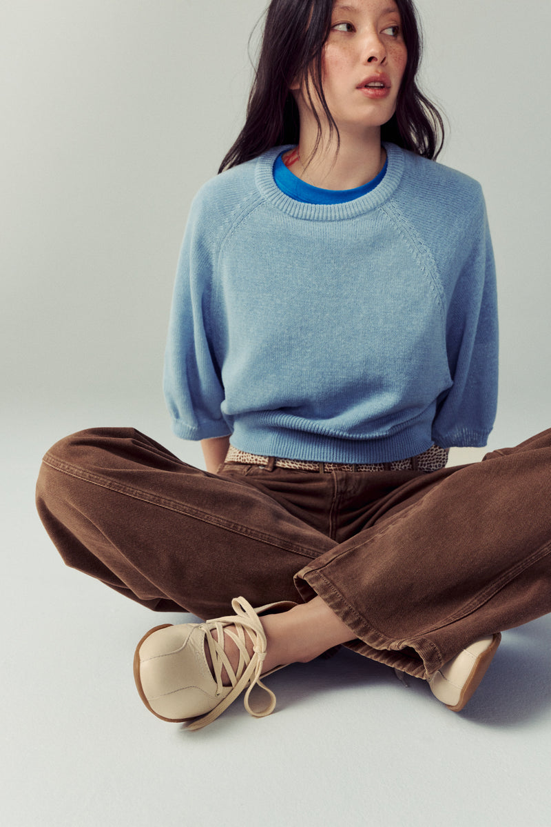 woman sitting down cross legged with brown jeans, blue sweater, and cream laced ballet flats