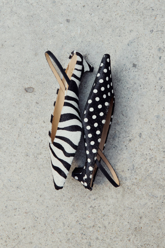 Pair of high-heeled shoes with zebra and polka dot patterns on a concrete surface.