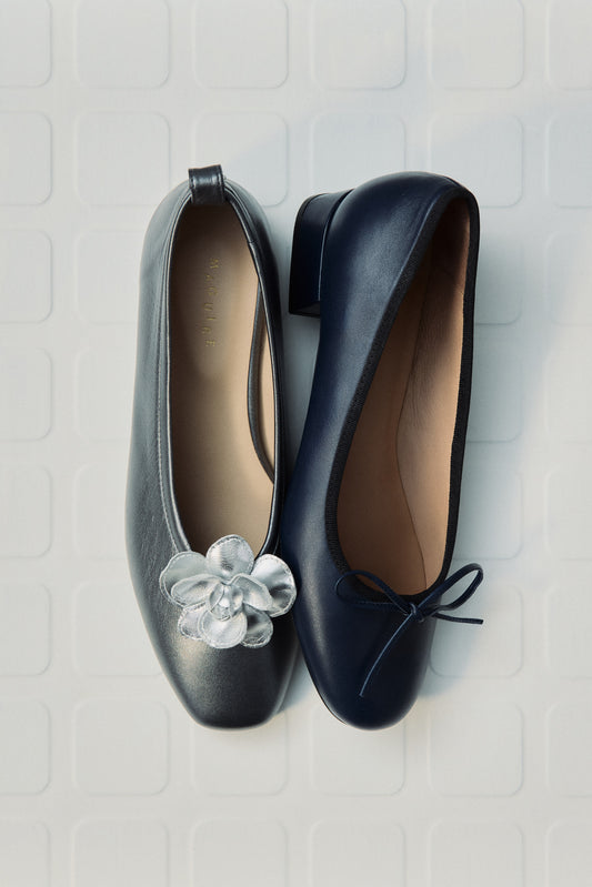 Grey and navy ballet flats on white textured background, grey ballet flat has a silver flower shoe clip on it