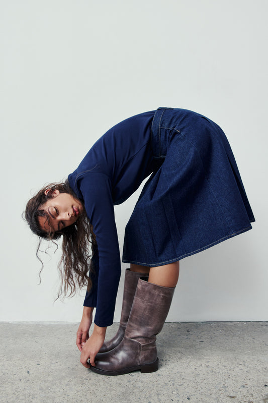 Person wearing a blue dress and brown boots against a plain background