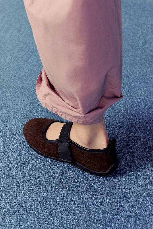 bottom half of a half, woman wearing dusty pink pants with brown flats on blue carpet.
