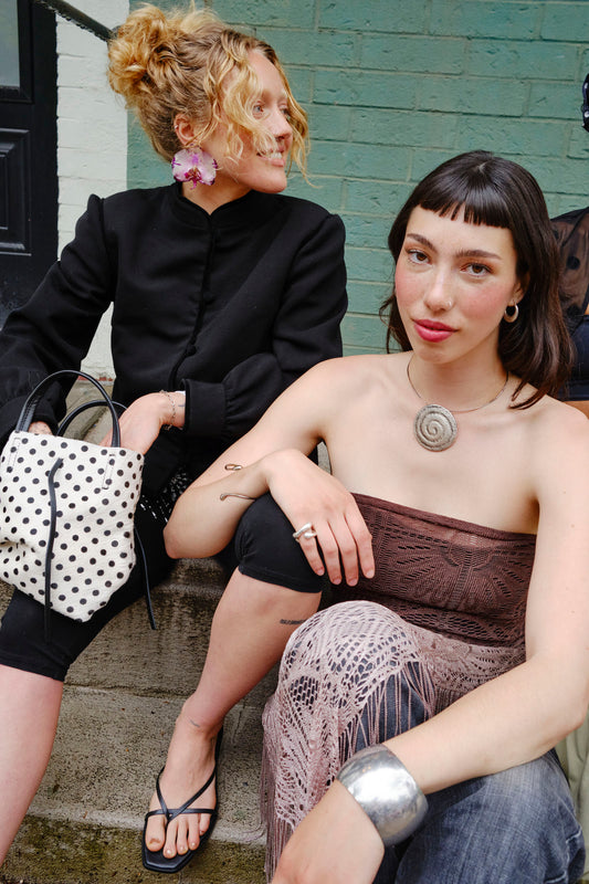 Two women sitting on steps, one holding a polka dot bag.