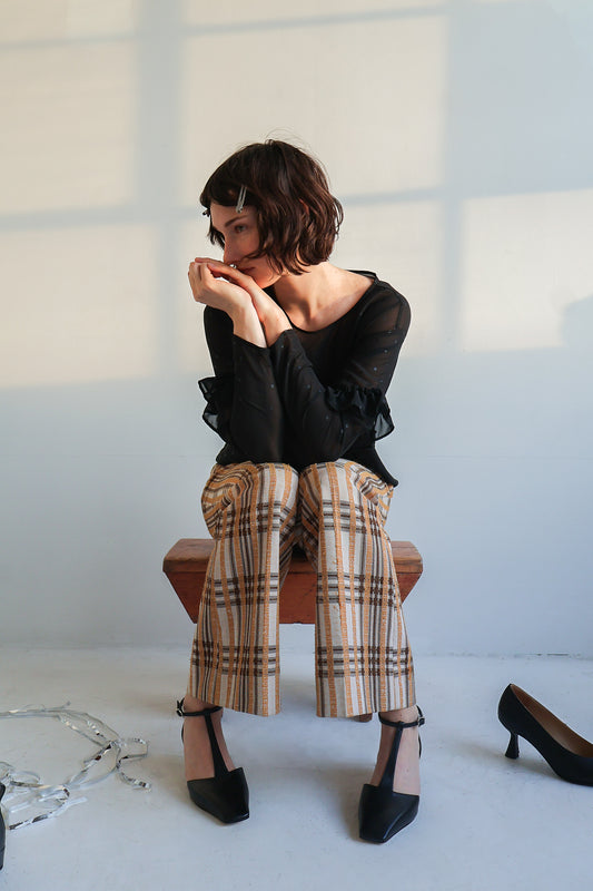 Person sitting on a stool wearing a black top, plaid pants and black t-strap kitten heels with a white background