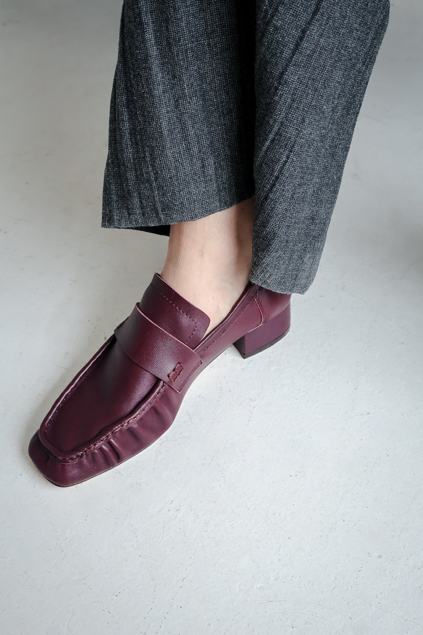 Bordeaux loafers worn with gray pants on a light background