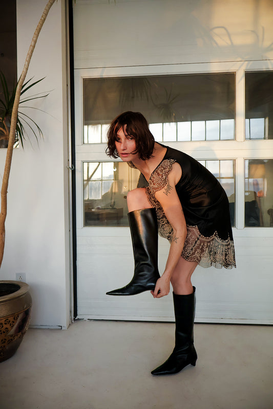 Woman wearing black knee-high boots and a black top with lace details in a modern indoor setting.