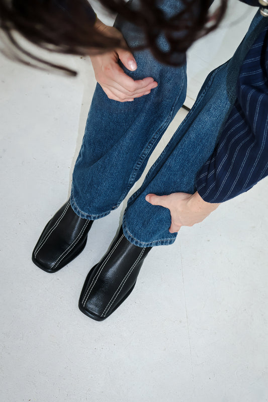 Woman bending down wearing jeans and black leather boots, hands on her knees and hair gracefully falling down.