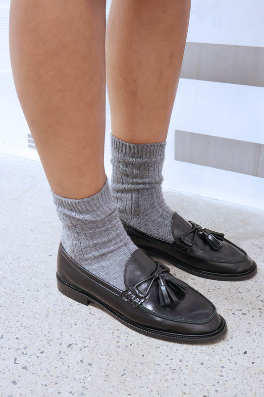 Black loafers with tassels worn with gray socks on a light background