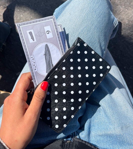 Person holding black wallet with white polka dots while sat down in the sun.