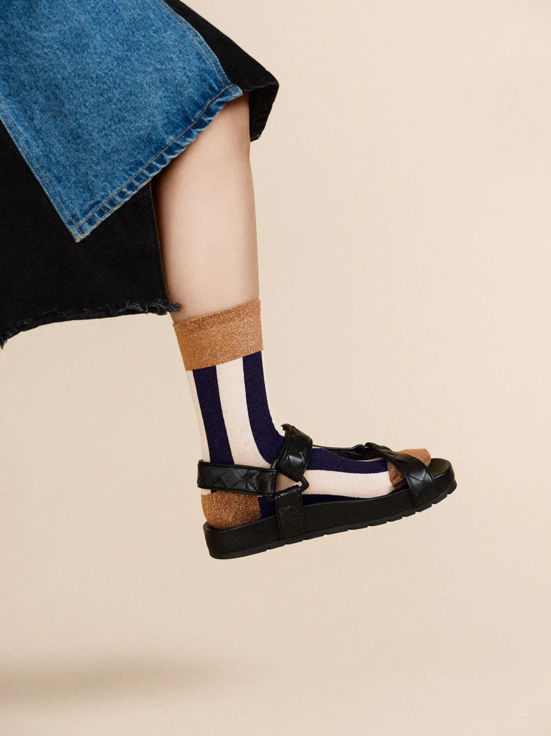 Black and white stripe sock with a gold edge. The model is wearing it with a sandal.