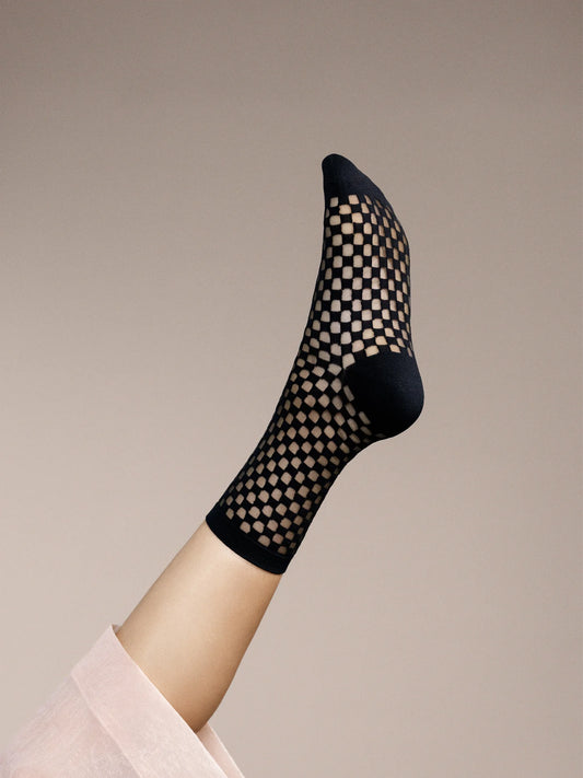 Black fishnet sock on a leg against a beige background