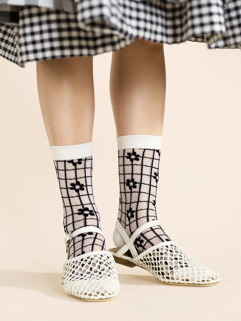 A pair of beige and black checkered socks with a floral pattern, worn with a black and white dress