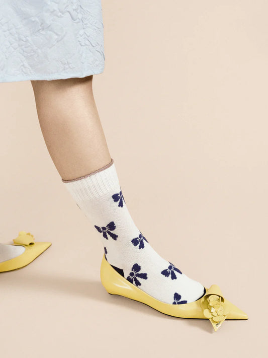 A pair of ivory crew socks with blue bows and yellow shoes, worn on a mannequin with a lacey blue dress .