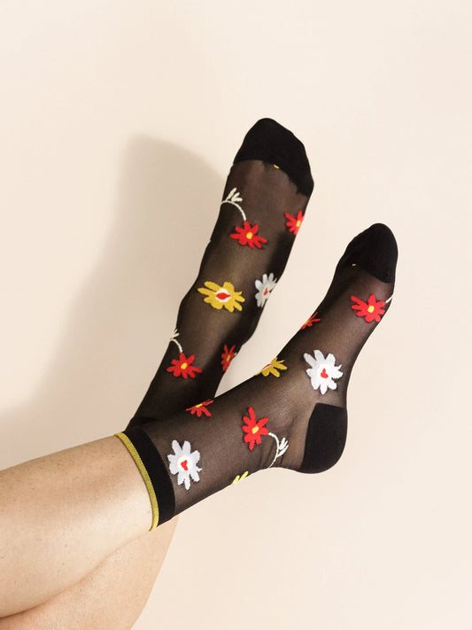 A pair of black sheer socks with a multicolored floral pattern, featuring a yellow trim at the top.