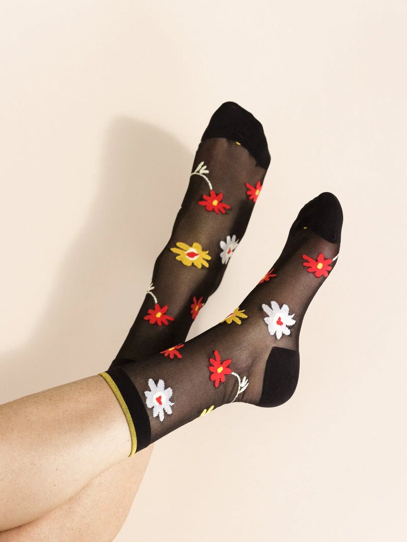 A pair of black sheer socks with a multicolored floral pattern, featuring a yellow trim at the top.