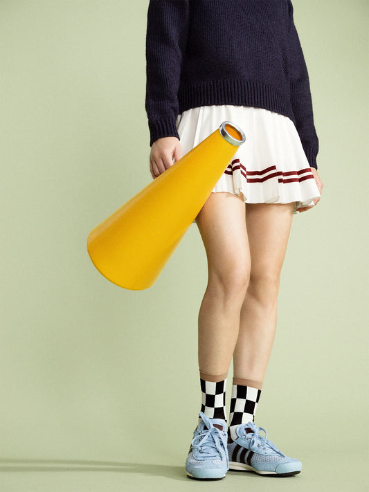 A person wearing a beige and red checkered sock, standing on a light green background.