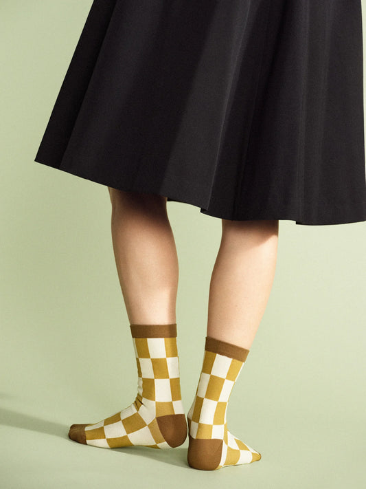 A person in a black skirt wearing checkered sock in tan, dark yellow and white.
