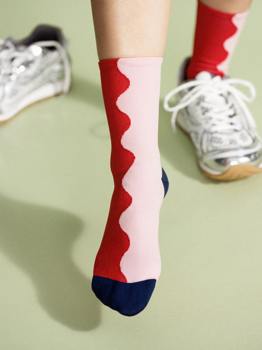 A person wearing silver sneakers and red and pink patterned socks standing on a green surface.