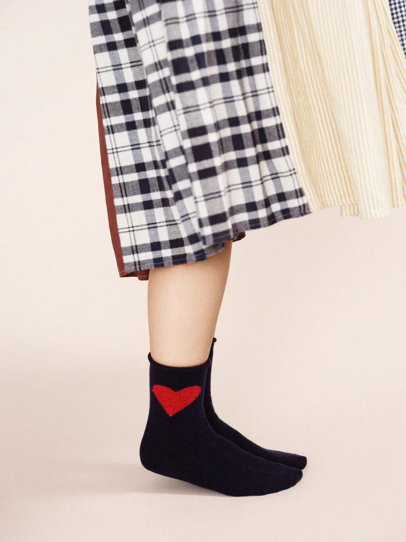 A pair of navy socks with a red heart emblem on the cuff, worn with a checkered skirt.