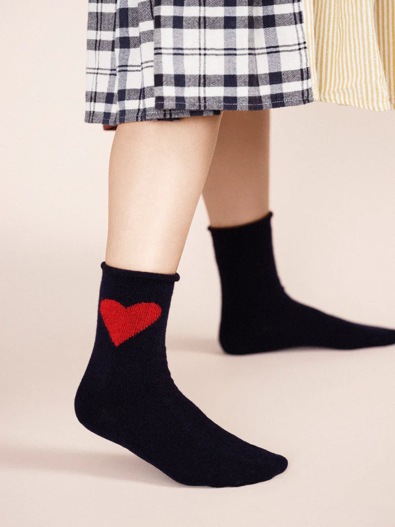 A pair of navy socks with a red heart emblem on the cuff, worn with a checkered skirt.