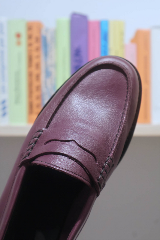 Purple loafer shoe with a blurred colorful bookshelf in the background