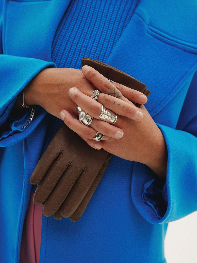 Model with bright blue coat holding a pair of taupe gloves.
