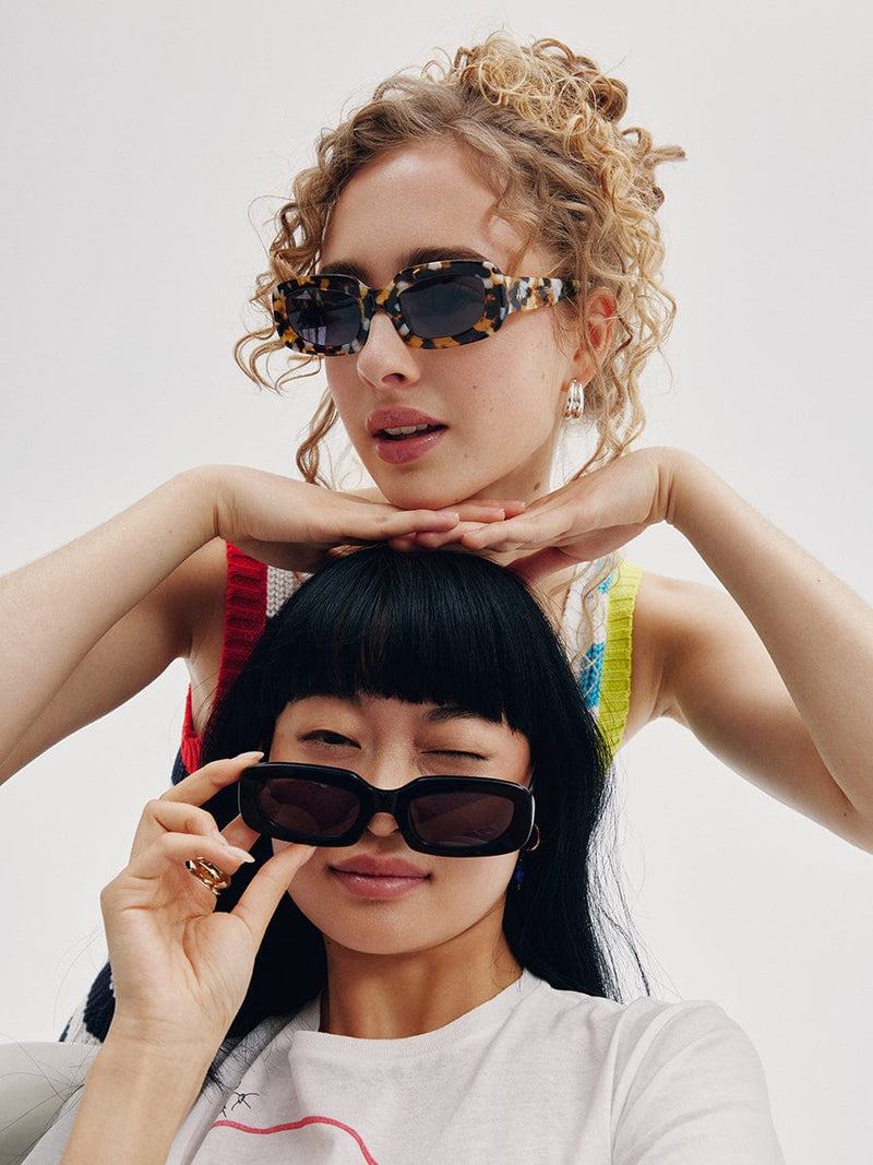 Asian model with black sunglasses and a multicolour t-shirt. Blond model with curly hair and tortoise sunglasses.